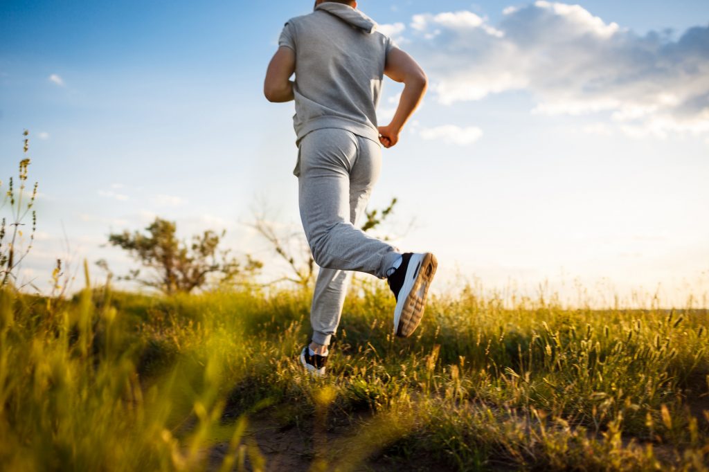 close up of sportive man jogging in field at sunrise